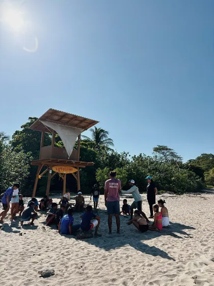 Grupo sentado en la arena junto a una torre de salvavidas
